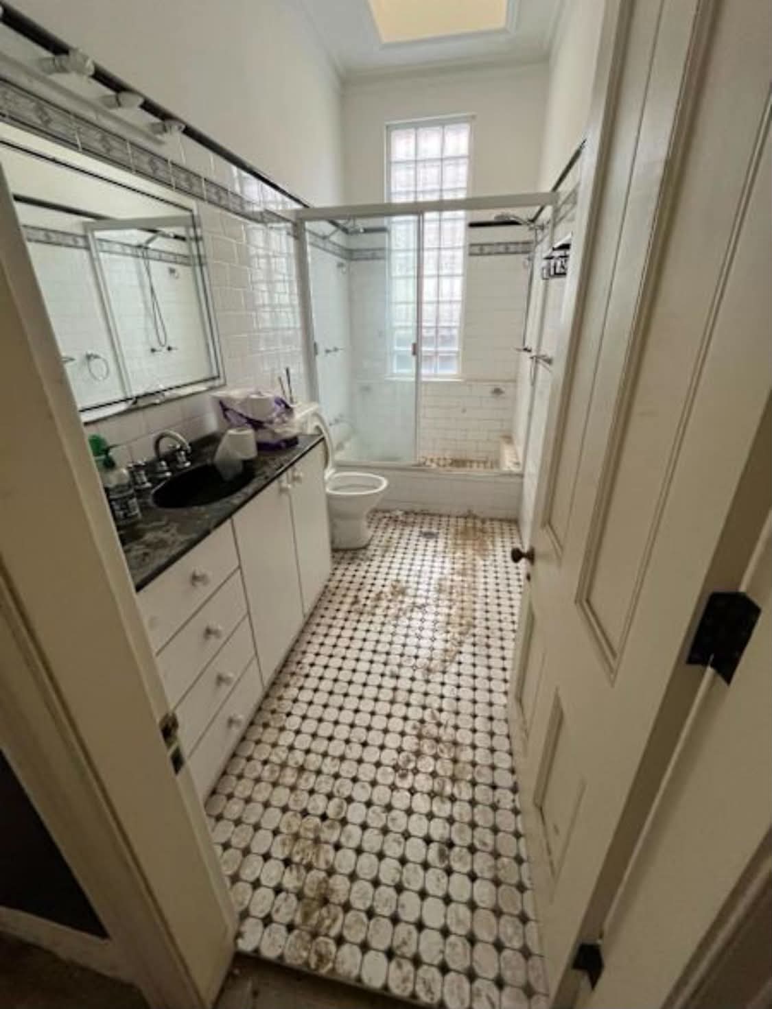 Tiled bathroom before stripout — vanity, mirror, shower screen, bath and mosaic floor tiles