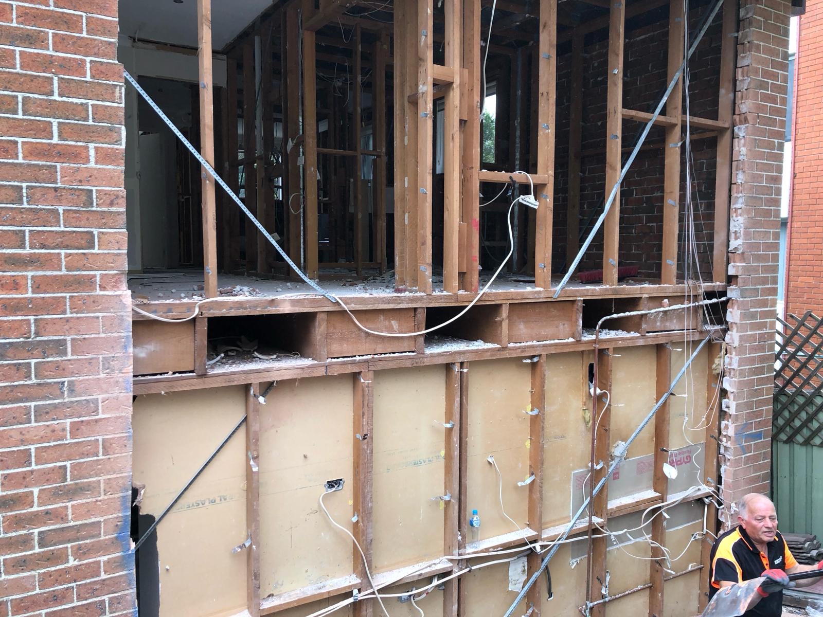 Two-storey brick home with rear wall stripped back to exposed timber stud frame