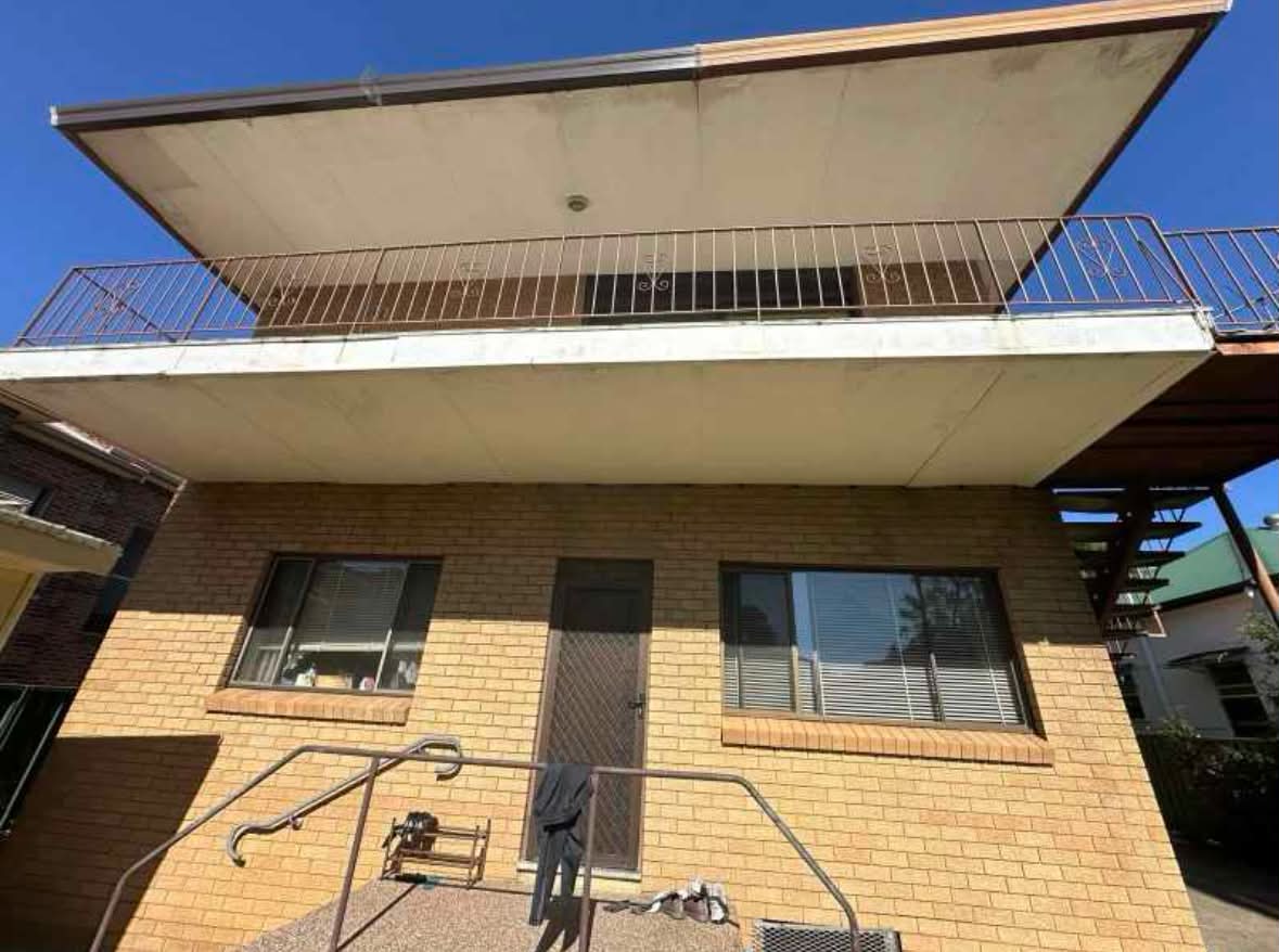 Two-storey brick home before demolition — enclosed upper balcony with awning and metal railing