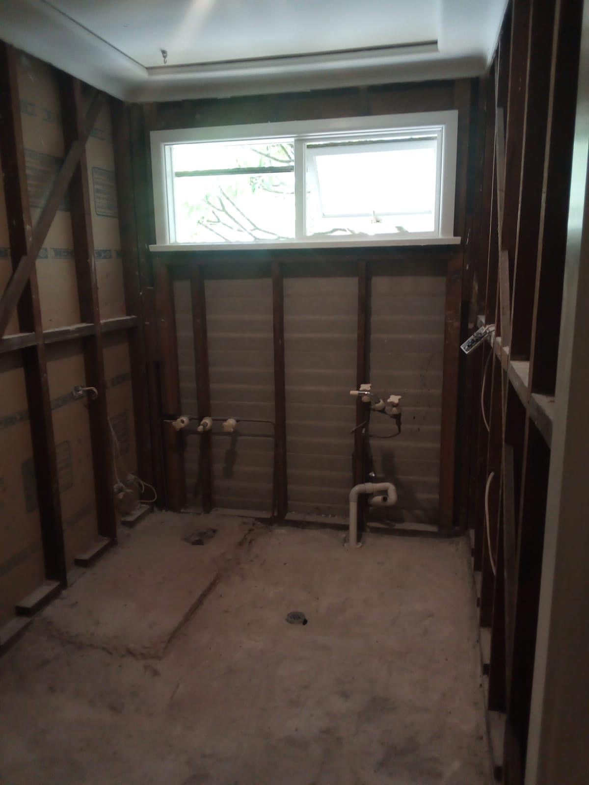 Bathroom after stripout — stripped back to bare timber stud frame with plumbing capped