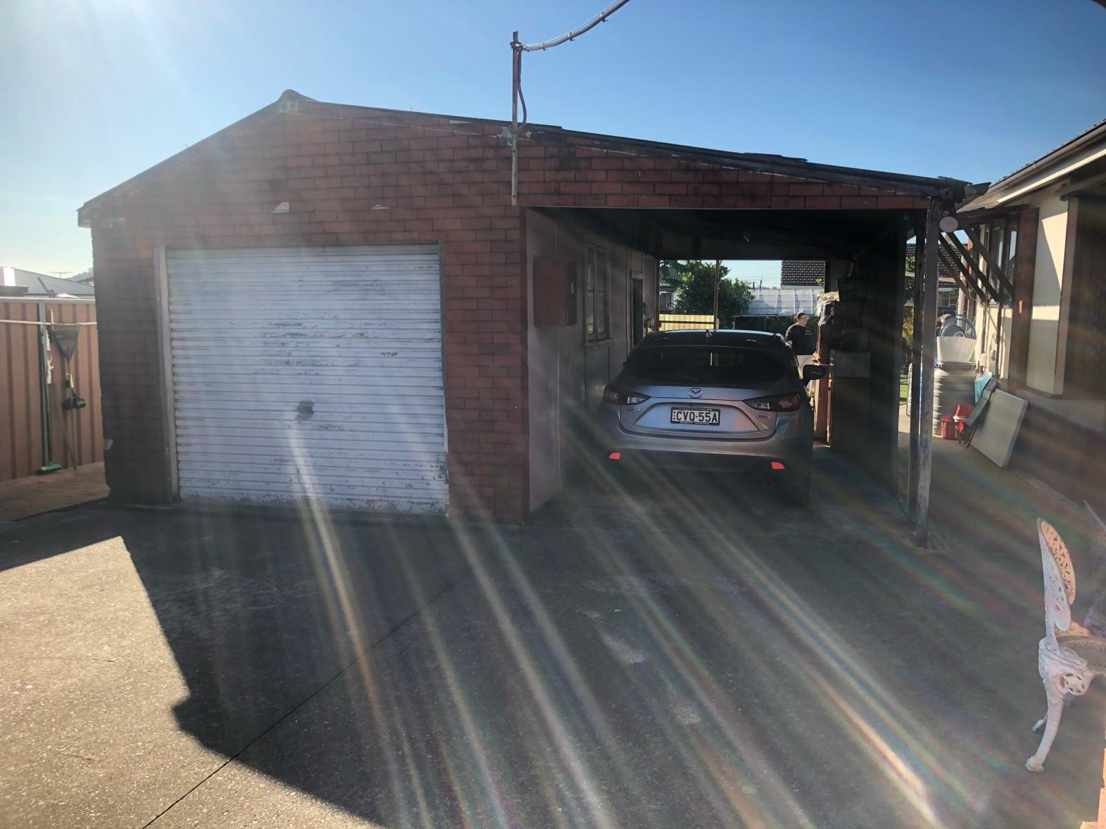 Brick garage and carport before demolition, vehicle parked under carport