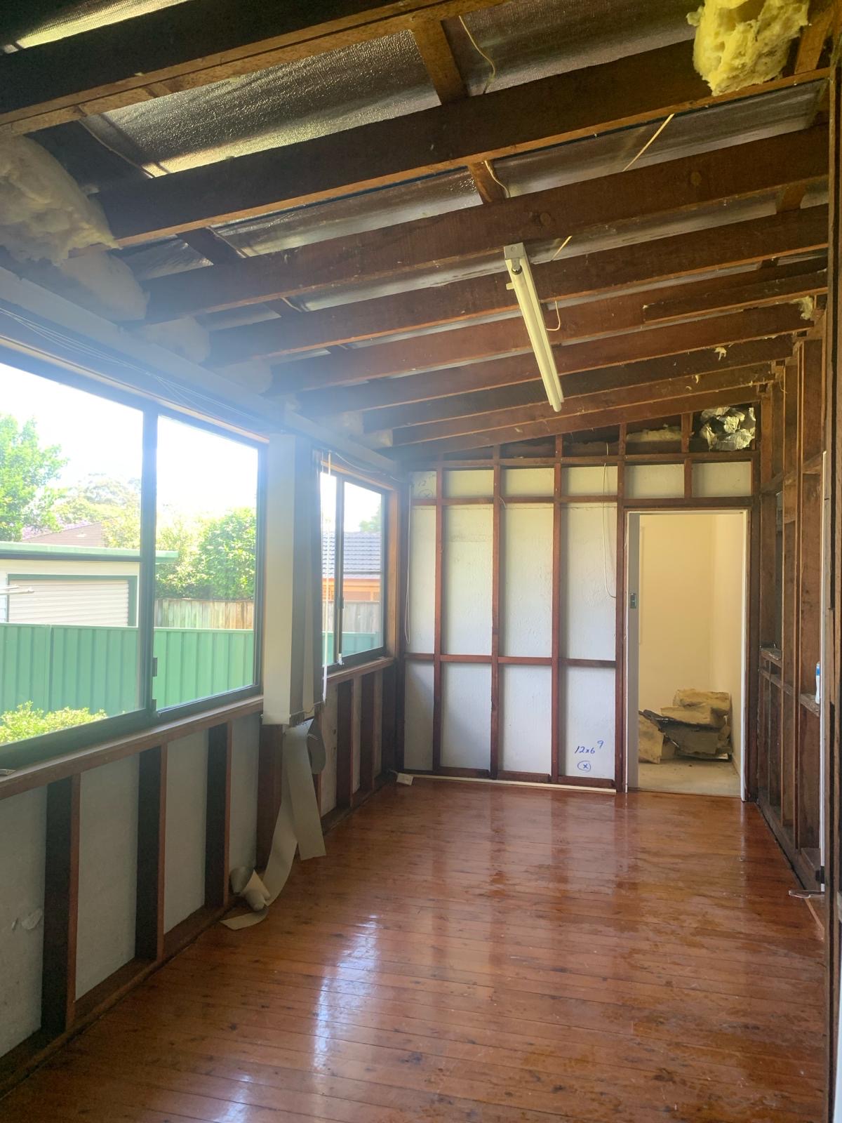 Sunroom after stripout — bare timber frame and rafters exposed, hardwood floor protected