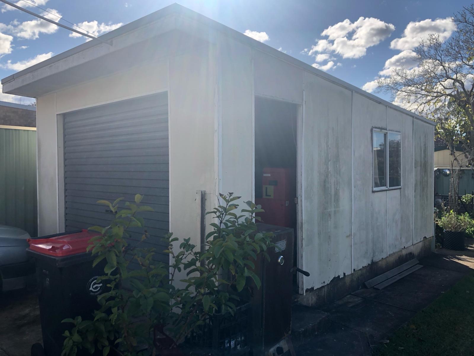 Clad backyard shed with roller door before demolition