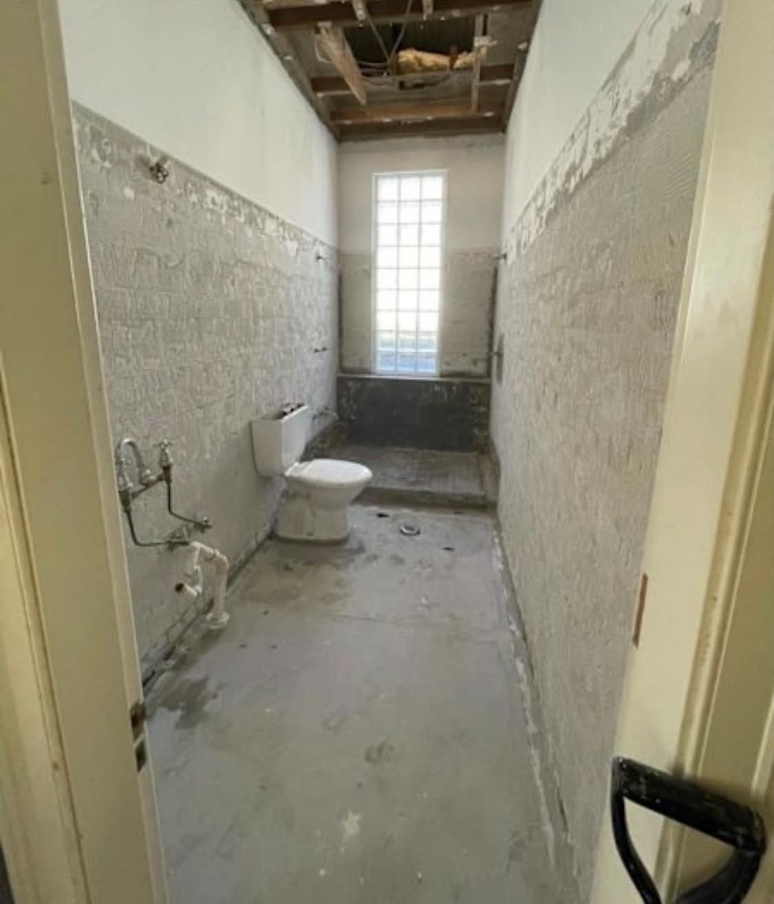 Same bathroom after stripout — tiles removed, fixtures out and ceiling opened for new services